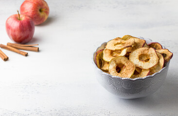 Homemade dried apples with cinnamon, apple chips in a bowl with cinnamon sticks on a light gray background. Delicious healthy snack