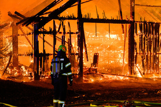 Ein Feuerwehrmann blickt auf einen in Vollbrand stehenden Stall