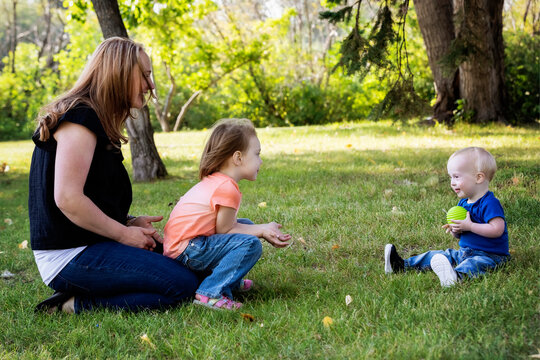 Mother throwing a ball with her daughter, and her young son who has Down Syndrome, in a city park during a warm fall afternoon; Leduc, Alberta, Canada