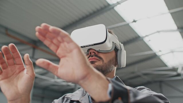 Camera view on Caucasian man with headset visualizing manufacturing products in factory. Engineer using VR glasses for productive work. Production with help of 3D vision. Technology innovation.