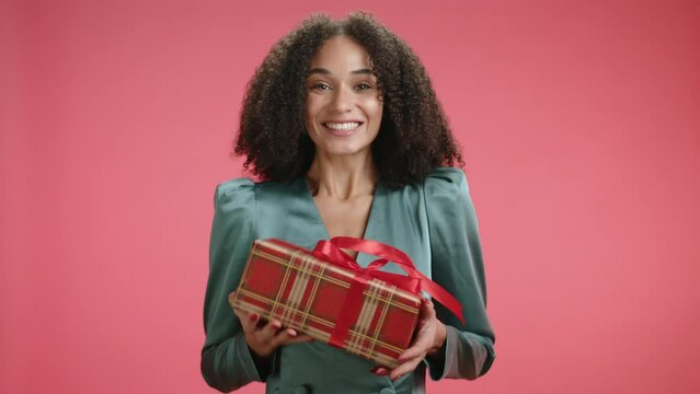 Extremely happy cute woman posing with Christmas gift wrapped into red checkered paper isolated on red background. Lady making faces, shaking with joy. High quality 4k footage