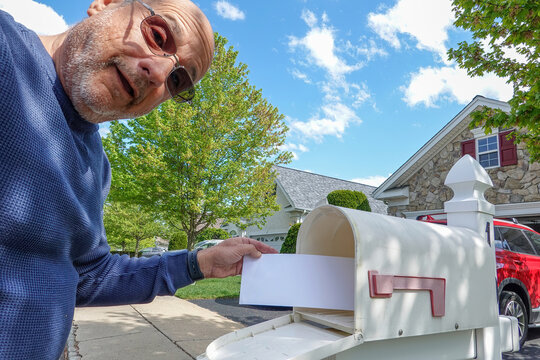 Happy senior citizen bald male takes an envelope out of his mailbox