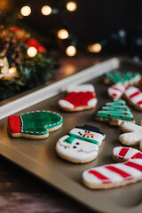 Christmas cookies on sheet or plate with golden lights on rustic table. Baking traditional snowman, tree, star cookies and santa hat.