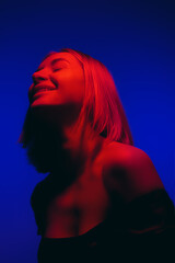 Upward gaze of a joyful woman illuminated by a serene blend of cobalt blue and crimson light