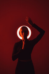 A woman's silhouette stands out against a circular halo light, creating a striking visual in red tones