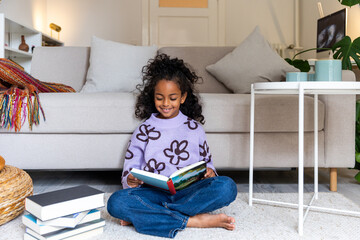 POC girl sitting in livingroom enjoying reading a book