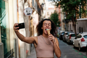 portrait of a young caucasian gay man with curly hair biting into an ice cream with an amused face...