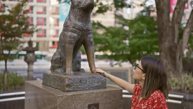 Alluring hispanic woman with glasses touches iconic hachiko statue on busy tokyo street – immersed in japanese culture and traditions