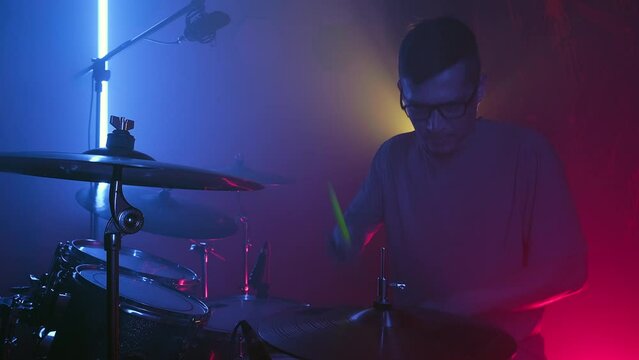 Close up male drummer emotionally hits the drums in neon lights. Music band rehearsal
