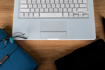 white laptop on a wooden table with blue agenda and graphic tablet, glasses on a white laptop, work...