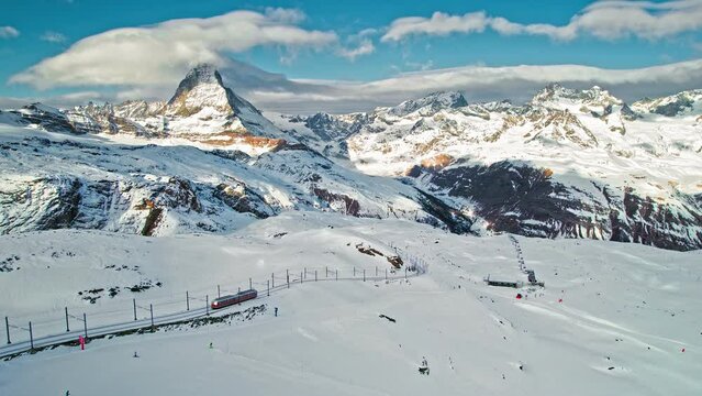 View from above of a passenger red train in the Matterhorn Alps in Europe, Switzerland. Aerial close-up view of a Swiss train with tourists on a railway and Matterhorn mountain in the background. 