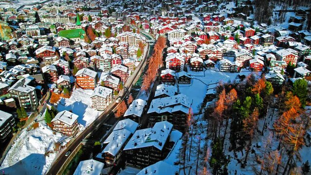 Aerial view of wooden Swiss houses and a Cathedral covered by snow in Zermatt. Ski Resort Town with typical Swiss buildings on hills with picturesque rivers in the Alps, Zermatt, Europe.
