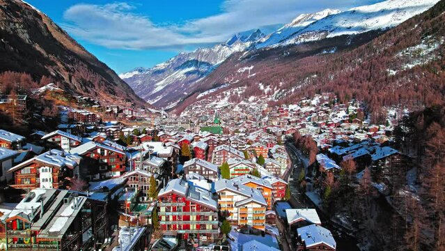 Aerial view of wooden Swiss houses and a Cathedral covered by snow in Zermatt. Ski Resort Town with typical Swiss buildings on hills with picturesque rivers in the Alps, Zermatt, Europe.