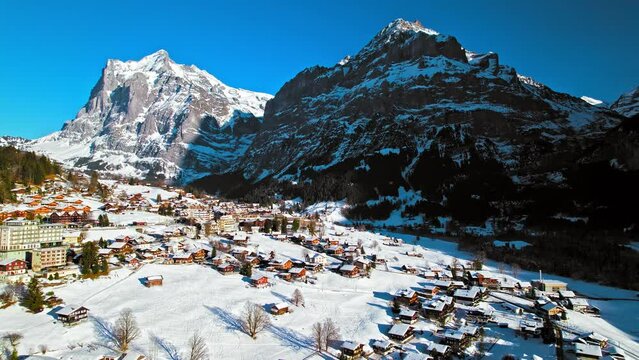 Scenic view from above of Grindelwald with colourful houses and the Bernese Alps in the background. Aerial view of glacier village and unique Alpine landscape at the foot of the Eiger north face.