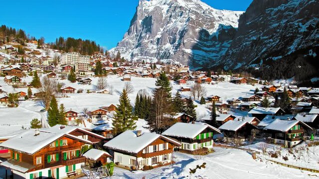 Scenic view from above of colourful wooden houses and the Bernese Alps in Grindelwald. Close-up aerial view of Swiss glacier village and unique Alpine landscape covered by snow in Switzerland.