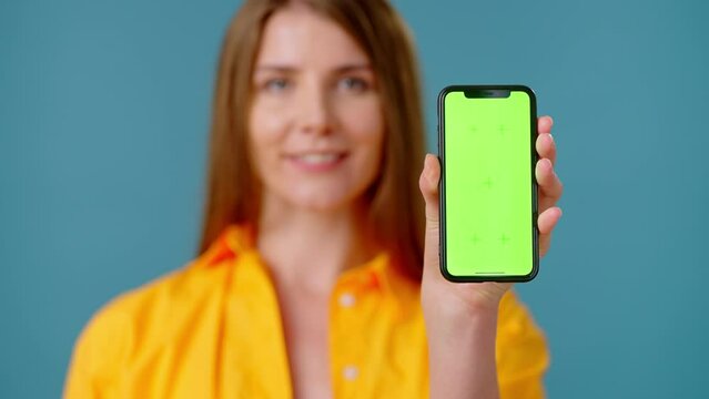 Friendly woman displays smartphone screen with chromakey