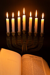 Holy Bible open to the Book of Genesis in Chapter 1 and Menorah with 7 lit candles isolated on dark...