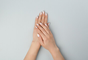 Woman with white polish on nails against light grey background, top view