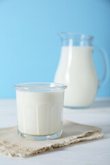 Glass of fresh milk and jug on white wooden table