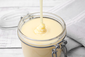 Pouring tasty condensed milk into jar on white table, closeup