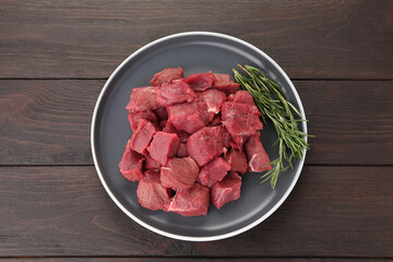 Pieces of raw beef meat with rosemary on wooden table, top view