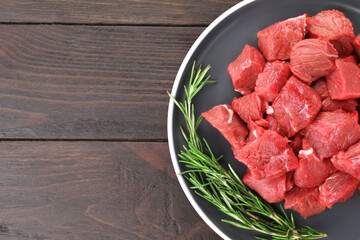 Pieces of raw beef meat with rosemary on wooden table, top view. Space for text