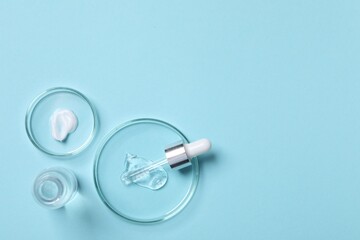 Petri dishes with samples of cosmetic serums, bottle and pipette on light blue background, flat lay. Space for text