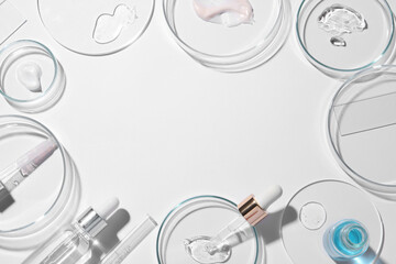 Frame made of petri dishes, samples of cosmetic serums, bottles and pipettes on white background,...