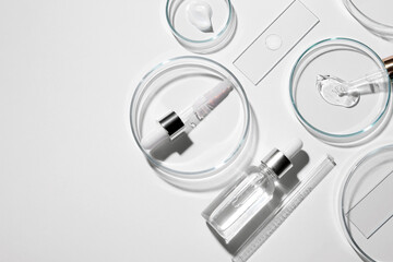 Flat lay composition with petri dishes and samples of cosmetic serums on white background. Space...
