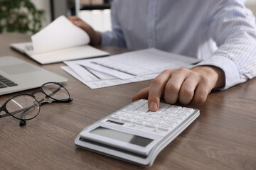 Man using calculator at wooden table indoors, closeup