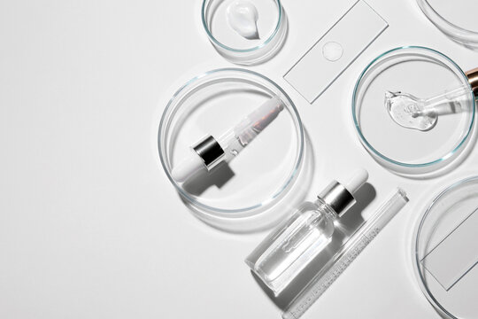 Flat lay composition with petri dishes and samples of cosmetic serums on white background. Space for text