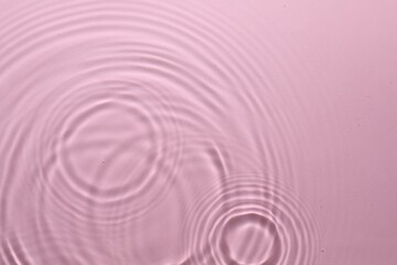 Rippled surface of clear water on pink background, top view