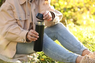 Woman opening thermos on green grass outdoors, closeup