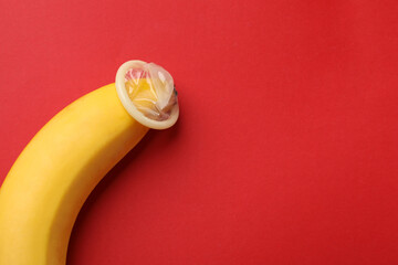 Banana with condom on red background, above view and space for text. Safe sex concept