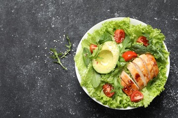 Delicious salad with chicken, cherry tomato and avocado on grey textured table, top view. Space for text