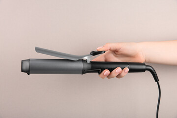 Hair styling appliance. Woman holding curling iron on light grey background, closeup