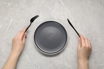 Woman holding fork and knife near empty plate at grey marble table, top view