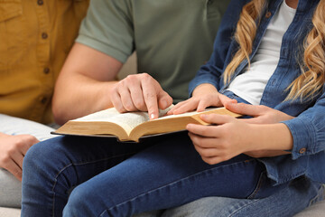 Girl and her godparents reading Bible together indoors, closeup