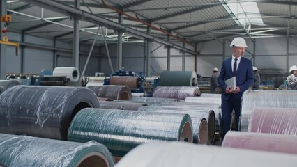 Attractive Caucasian man with helmet and elegant suit holding laptop while walking in facility. Successful director considering products. Controlling working process. Management concept.