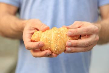 A man's hand holds a croissant, snack and fast food concept. Selective focus on hands with blurred background