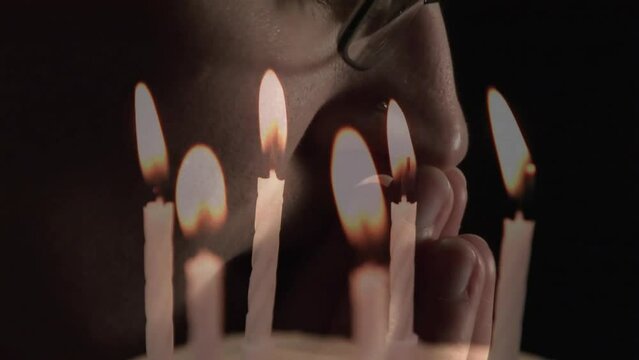 Animation of burning candles over man praying on black background