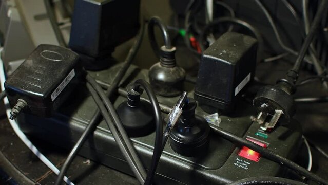 Black unsafe cluttered 240 volt electric Surge protector power-board  chargers frayed power leads cords crossed over each other with movement 