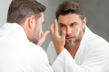 Obraz premium Male cosmetic. Beauty man applying face cream. Skin care cosmetic. Male cosmetics face cream. Facial cream, moisturizing lifting creme. Face cream for skincare. Wrinkle cosmetic facial treatment.