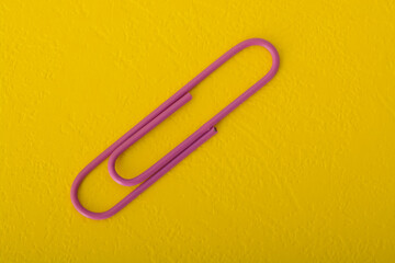 Purple paper clip isolated on a yellow background.