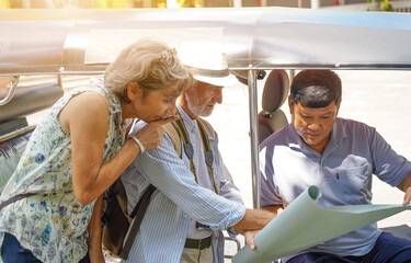 Closeup American senior tourist man with his friend European ask the Tuktuk Thailand taxi driver for them destination on the map with sun bright background. Senior tourist concept