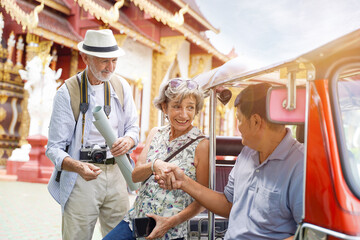 European senior tourist woman are congratulatory handshake with the Tuktuk Thailand taxi driver on Thai temple background. Senior tourist concept - obrazy, fototapety, plakaty