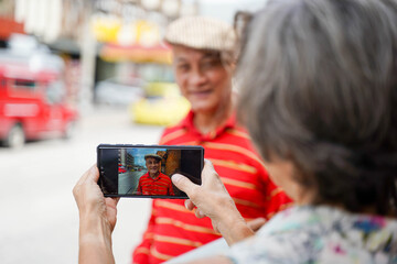 Closeup back view of senior tourist woman take a photos to her friend by smart phone while walking around the city on blurred of city background. Senior tourist concept