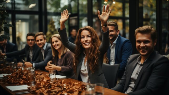 A group of people are gathered around a table strewn with autumn leaves, woman in the center raises her hands with excitement, signifying a joyful celebration or team success, corporate event, team