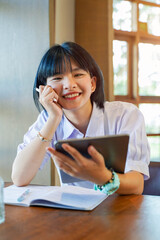 Closeup and front view of happiness cheerful Thai girl student holding a tablet with studying in the classroom on sun flare background. Network education concept.