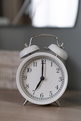 Close-up of a round white alarm clock on a table in the bedroom. The hands on the clock show seven o'clock in the morning, time to get up. Retro alarm clock on the table, vintage tone. space for text